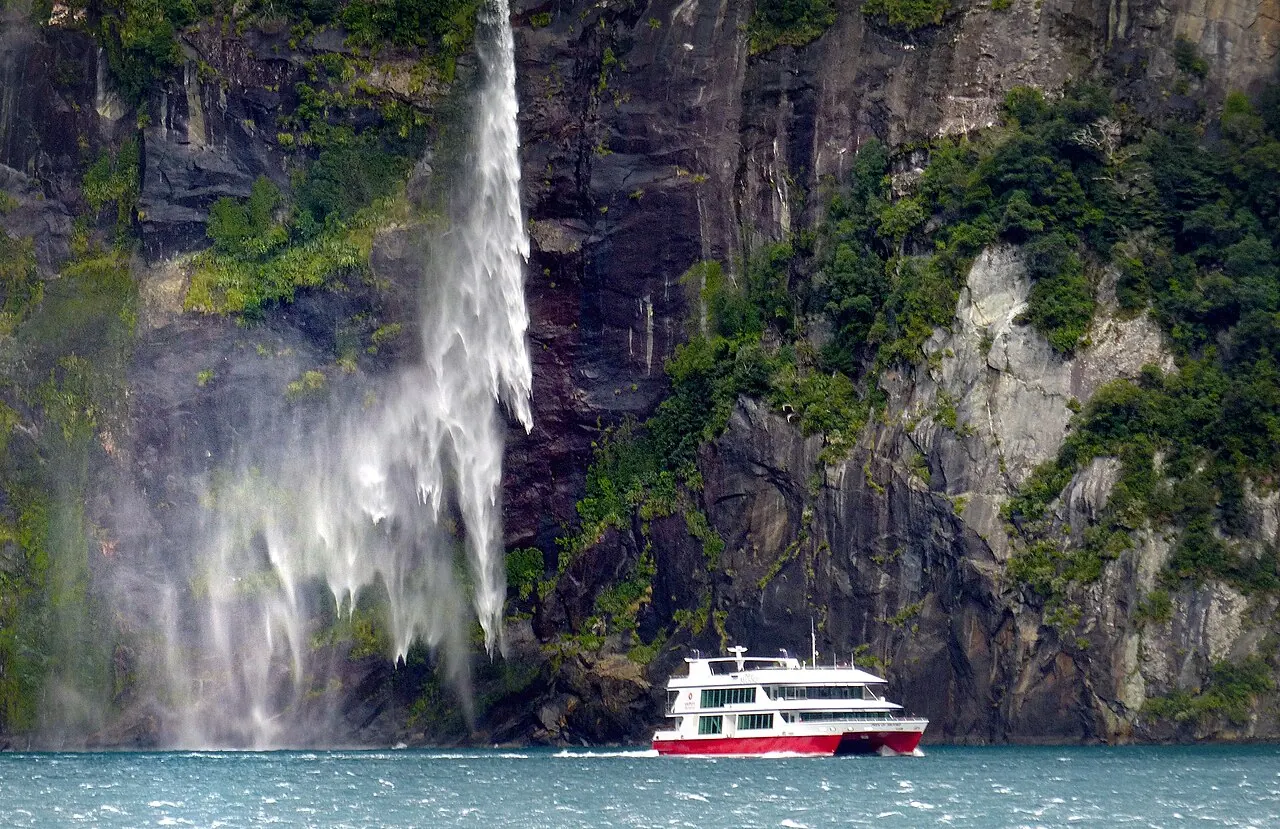 A waterfall pouring into Milford Sound beside a cruise